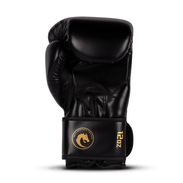 Rear (palm) view: smooth black synthetic-leather with stitched grip bar, ventilated finger gussets, and circular gold dragon badge on wrist cuff (12 oz).