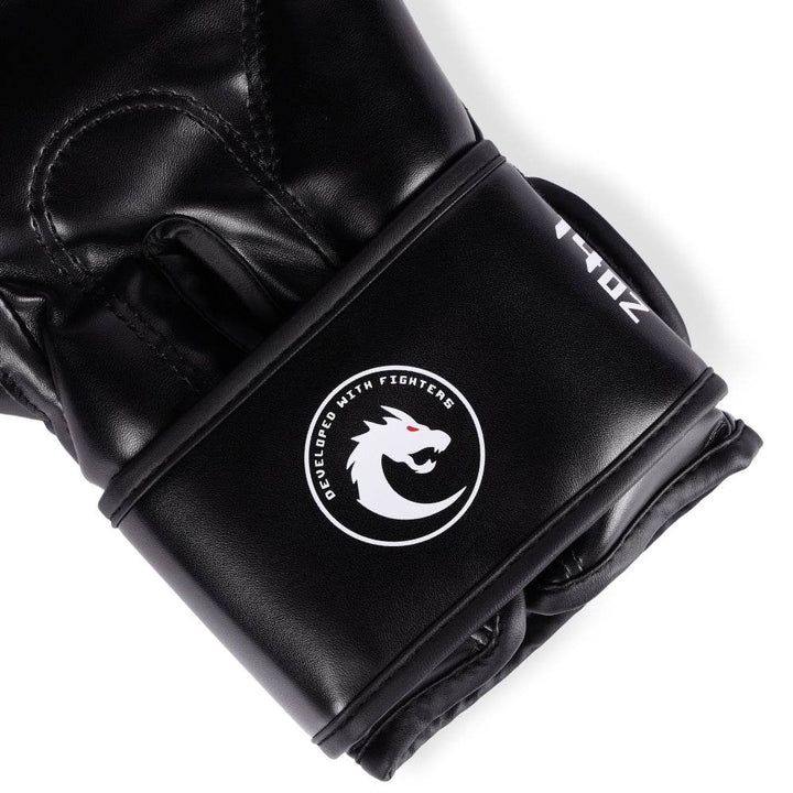 Macro of underside wrist strap: white “12 oz” weight stamp and round “Developed With Fighters” dragon crest on satin-finish black leather.