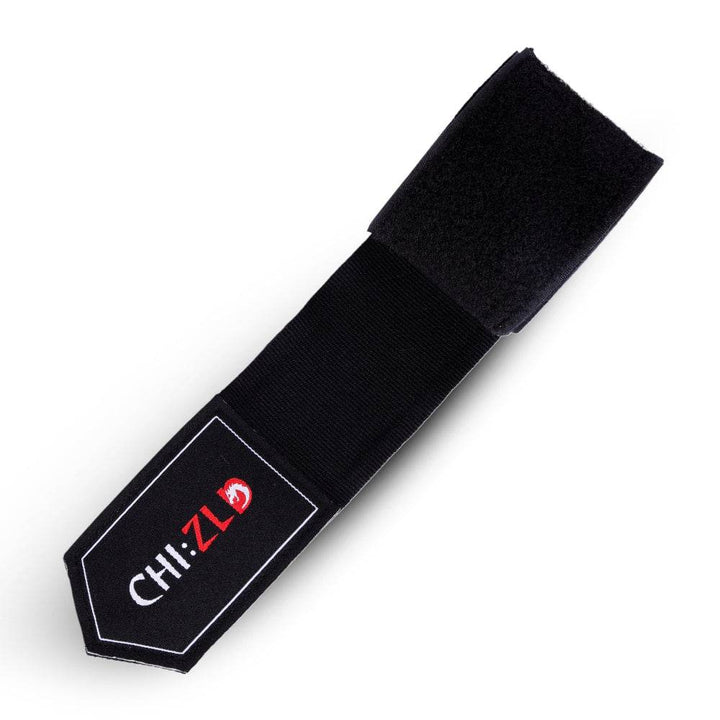 Angled view of partially unrolled wrap: vivid black elastic band with black patch and logo, end secured by wide black Velcro strip.