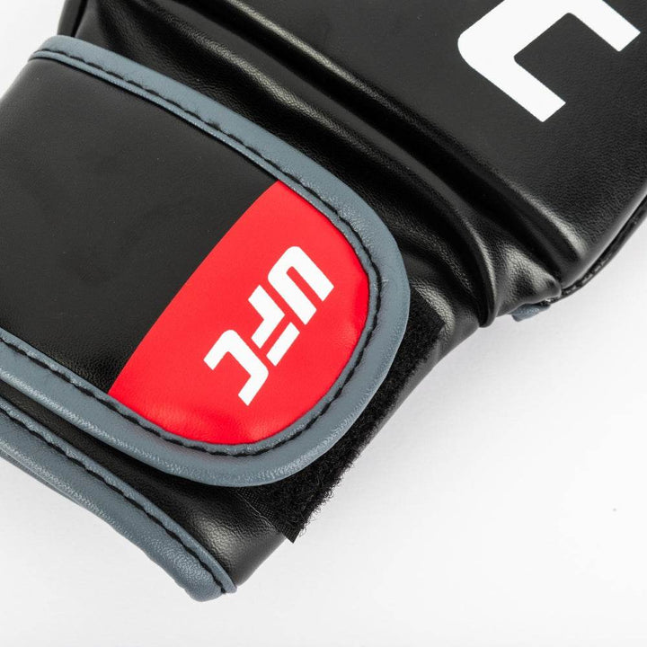 Macro of strap tab: black panel with subtle octagon icon, framed by vivid red stitched border and smooth grain texture.