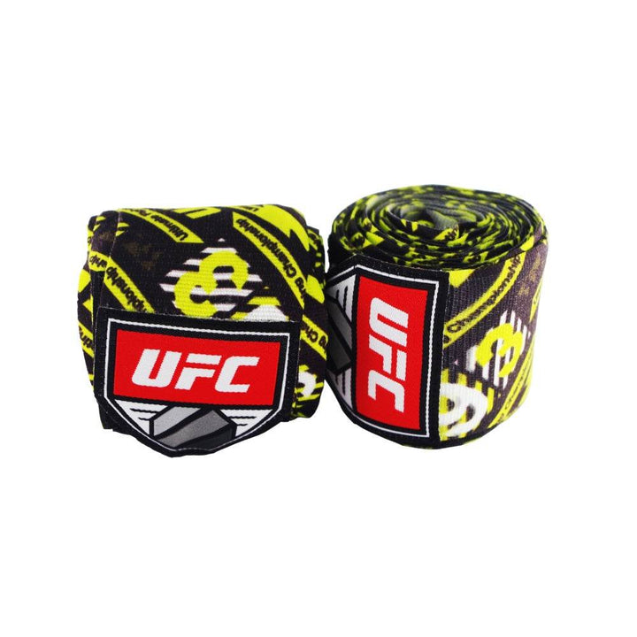 Pair of rolled UFC 4.5 m hand wraps in a black-and-fluorescent-yellow graffiti pattern with repeating UFC text; bold red-and-white UFC shield logo patch visible on each roll.
