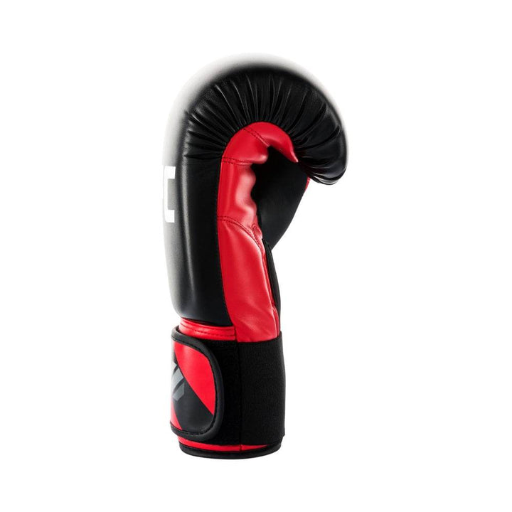 Side profile of a red-and-black UFC Pro Compact bag glove laid on its outer edge, emphasizing the curved glossy black knuckle panel with bold red “UFC” logo, padded red wrist cuff, and partially visible black ventilated palm mesh.