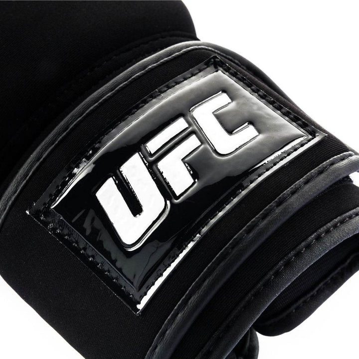 Close-up of the glossy black rubberized wrist patch with raised white “UFC” lettering stitched to the strap.