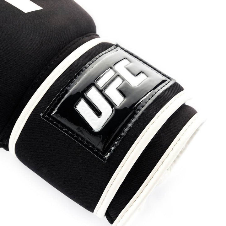 Close-up of the glossy black rubberized wrist patch with raised white “UFC” lettering stitched onto the hook-and-loop strap.