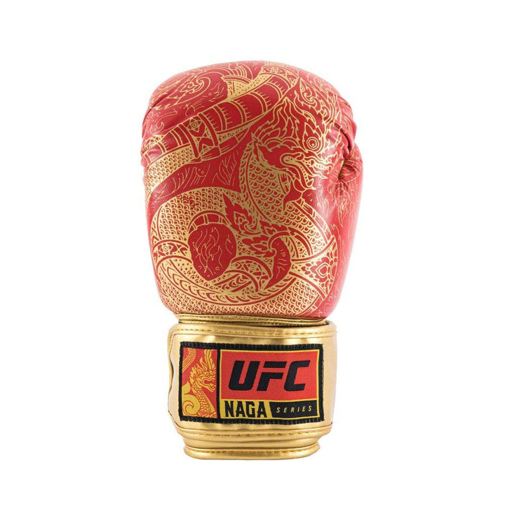 Front-angle view of a red UFC Thai Naga boxing glove standing upright, featuring a stylised black Naga (serpent) scale graphic across the knuckle area and a contrasting black hook-and-loop wrist strap with UFC branding.