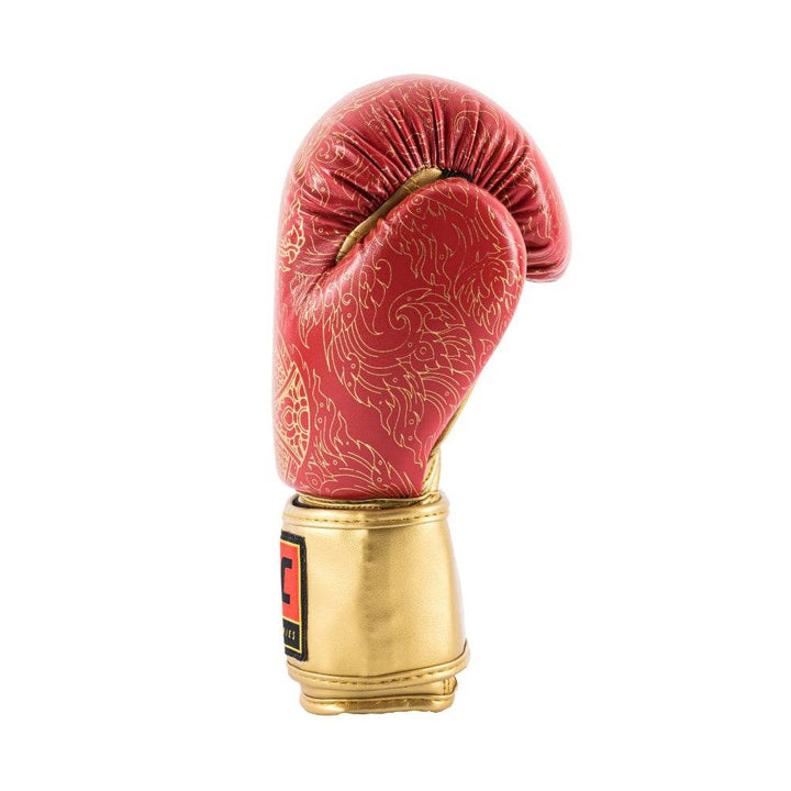 Close-up view of the red UFC Thai Naga boxing glove’s thumb and wrist area, showing the textured black serpent-scale graphic curving over the thumb joint, precise red stitching, and the black hook-and-loop wrist strap with reinforced edge binding.