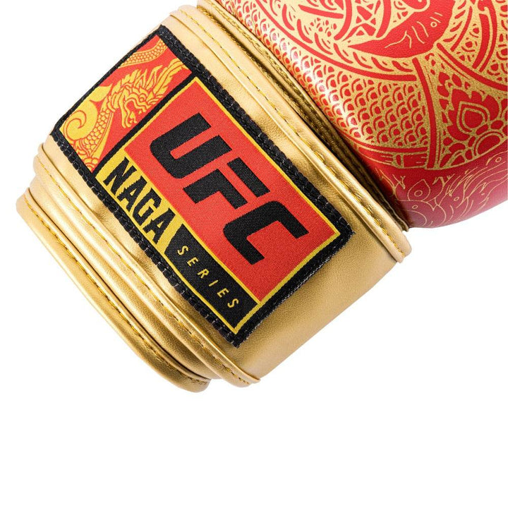 Close-up of the wrist enclosure on a red UFC Thai Naga boxing glove, showing the black hook-and-loop strap with stitched UFC logo tab and a glimpse of the red knuckle area featuring the snake-scale graphic.