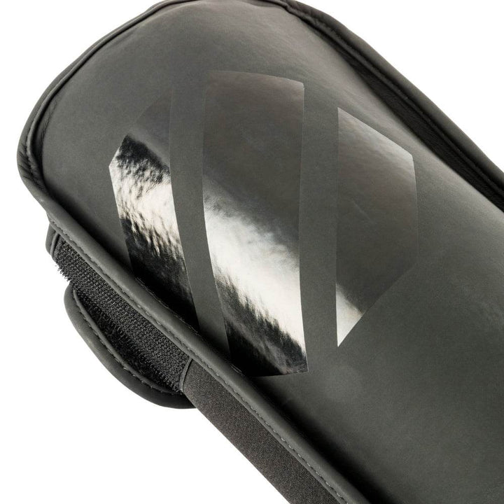 Close-up – shin panel finish: Detail of the front strike surface highlighting the subtle glossy octagon logo printed on the otherwise matte synthetic leather.