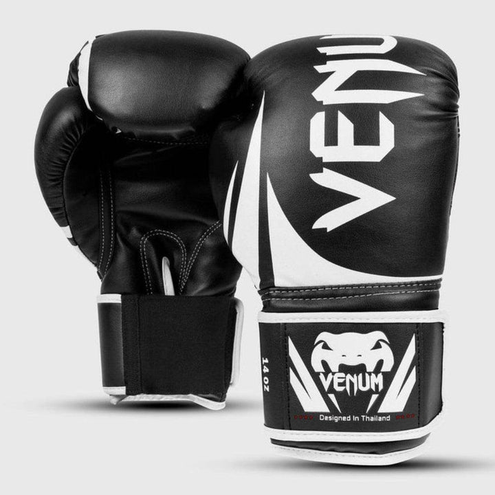 Front and side view of the Venum Challenger 2.0 boxing gloves in black and white, showcasing bold Venum branding on the punch surface and white snakehead logo on the wrist strap marked “14 OZ.”