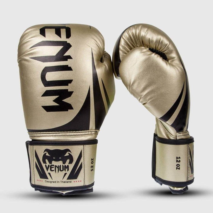 Front and side view of Venum Challenger 2.0 boxing gloves in metallic gold with black accents, featuring the large vertical VENUM logo and black snakehead emblem on the wrist strap marked “12 OZ.”