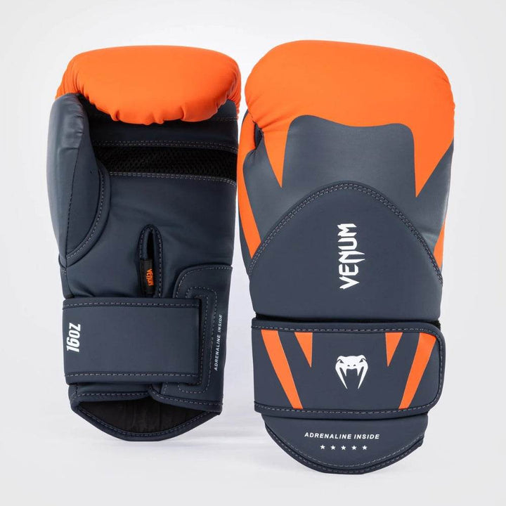 Both gloves displayed upright showing the orange top padding and grey synthetic leather with angular orange streaks and the Venum logo.