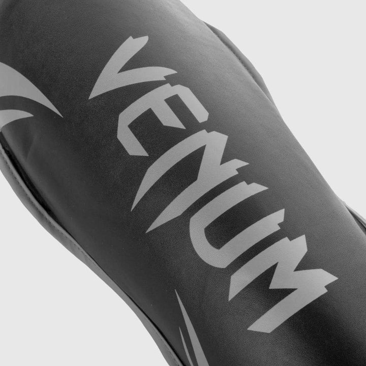 Close-up of Venum logo printed in grey on black challenger shin guard surface, showing texture and branding clarity.