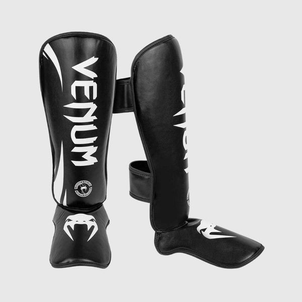 Black and white Venum Challenger Standup Shinguards displayed side-by-side in a three-quarter angled view showcasing branding and foot protection padding.