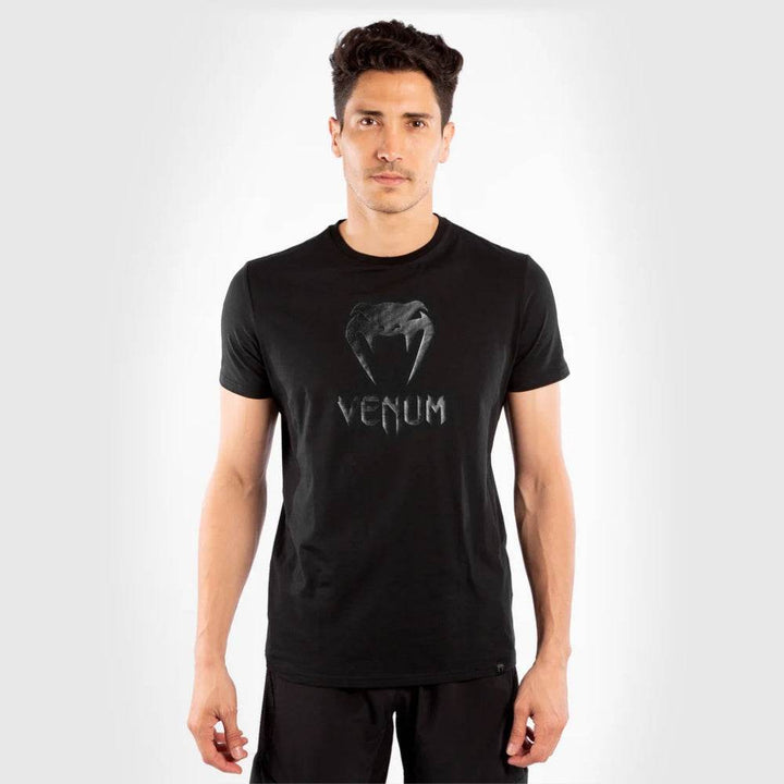 Man standing front-facing, wearing a black Venum t-shirt with a glossy black Venum logo on the chest.