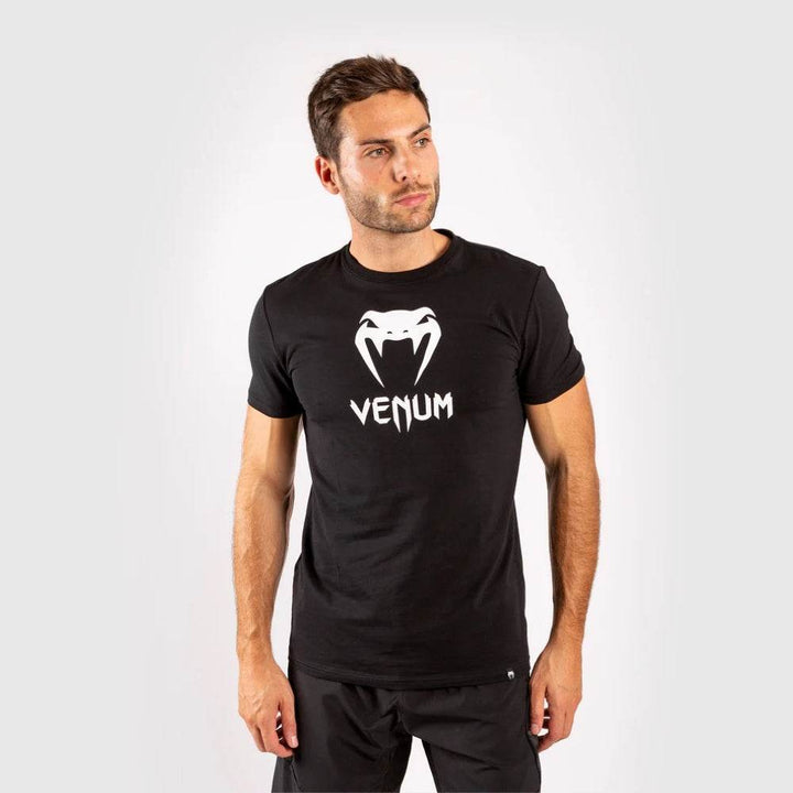 Man wearing a black Venum logo t-shirt and black shorts, facing forward with a neutral expression.