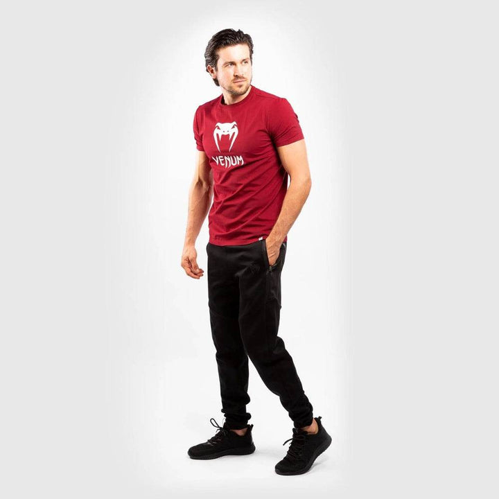 Full-body shot of the man in a red Venum shirt and black joggers, hands in pocket, in a dynamic stance.