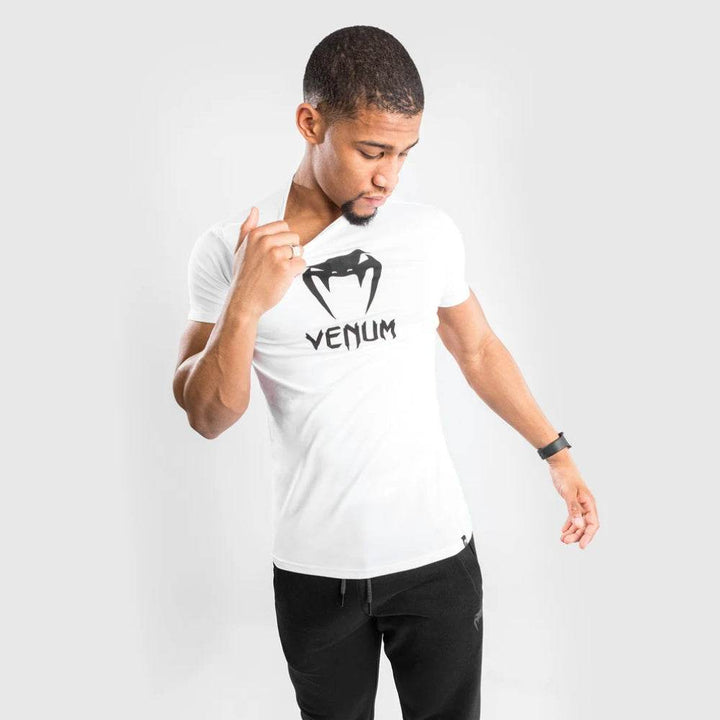 Man looking down and tugging on his white Venum logo t-shirt paired with black joggers.