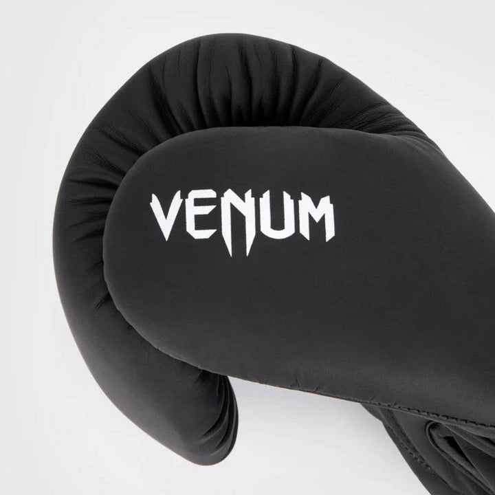 Close-up side view of the black/white Venum Contender 1.5 boxing glove showing the thummb area with "VENUM" branding on the thumb and smooth synthetic leather finish.