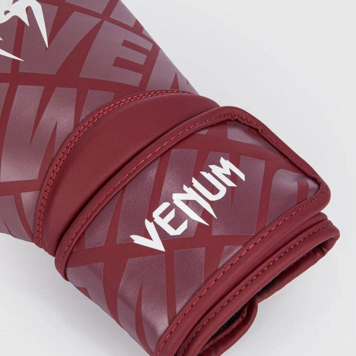 Detailed close-up of the burgundy glove’s wrist strap area showing white “VENUM” print and reflective surface.
