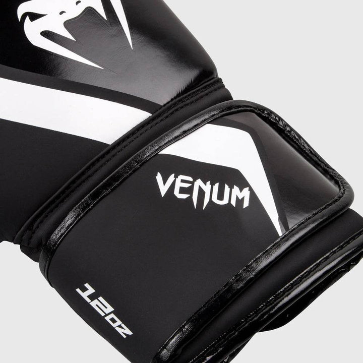 Close-up of the glove's wrist area highlighting the angular white Venum logo and glossy black trim over the matte black strap with visible “12oz” marking.