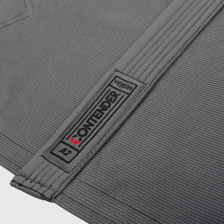 Detailed shot of Venum Contender label on grey jacket, placed on textured fabric.