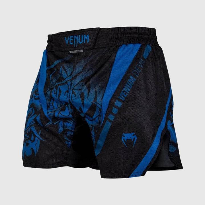 Black fight shorts with blue tribal Oni mask graphic covering the front panels, blue Venum logo on waistband and left leg, and contrasting side panel.