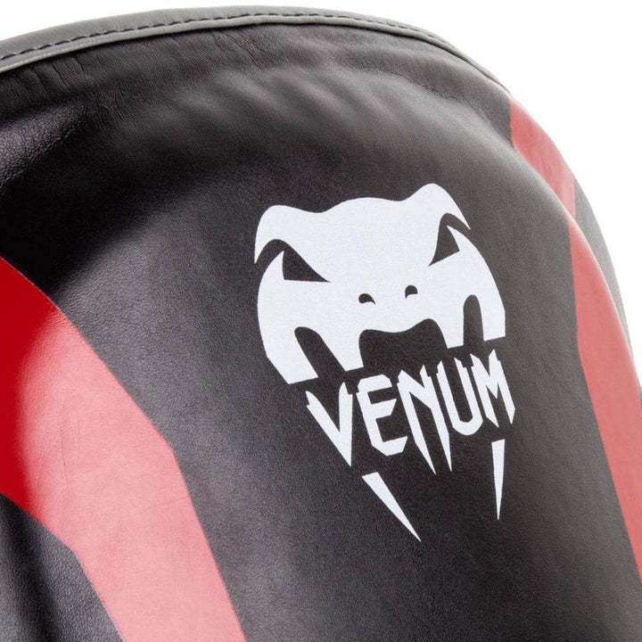 Close-up of the white Venum logo printed on the front center of the belly protector against black and red synthetic leather.