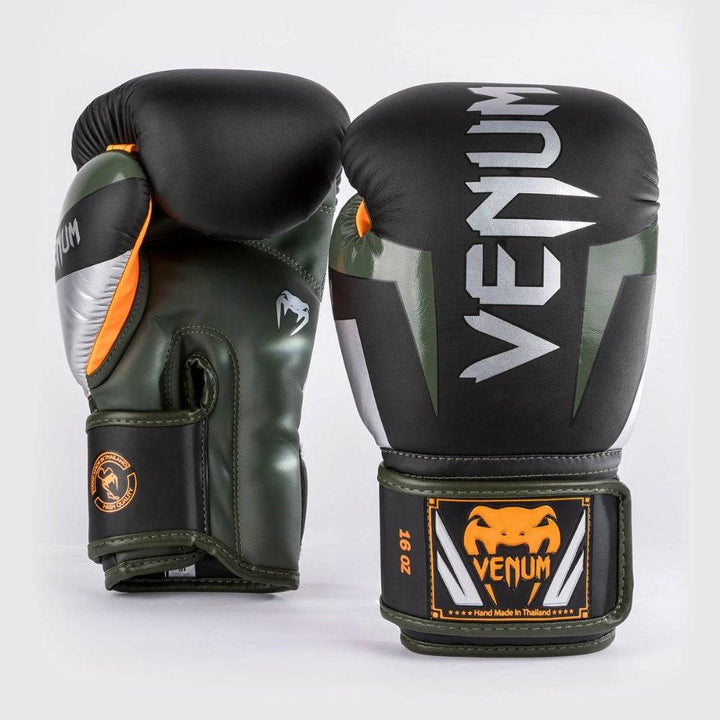 A pair of Venum Elite boxing gloves in black, silver, and kaki green with orange accents, displayed upright showing the Venum logo and 16oz size.