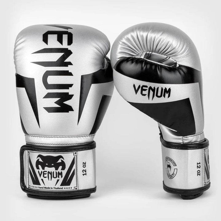 Front and side facing view of Venum Elite boxing gloves in silver and black. The gloves feature a sharp black pattern on the knuckle area and the signature “VENUM” text vertically and same on the thumb.