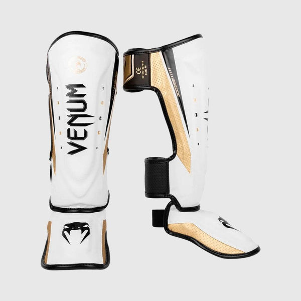 Front and side view of Venum Elite Evo standup shinguards in white, gold, and black, featuring Venum branding on the shin and instep protection.