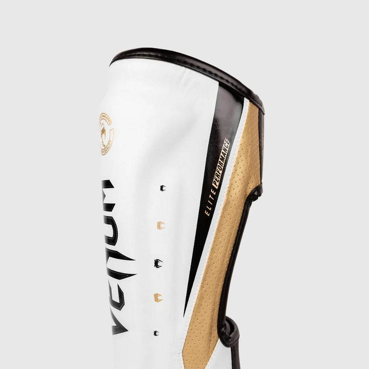 Close-up of the upper shin section of a Venum Elite Evo shinguard showing "Elite Performance" text detail along gold mesh and black trim.