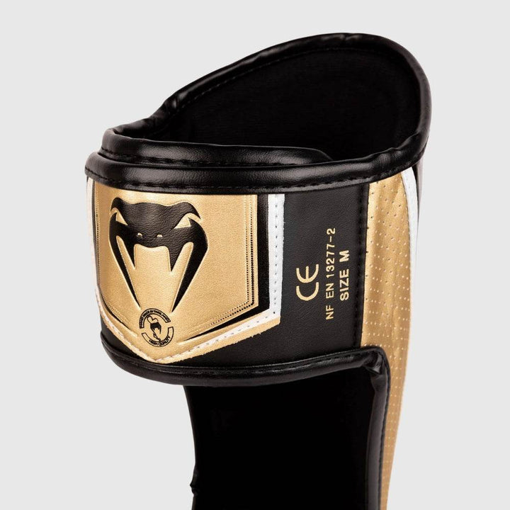 Close-up of the rear velcro strap on the Venum Elite Evo shinguards with gold and black Venum snake logo patch and CE certification.