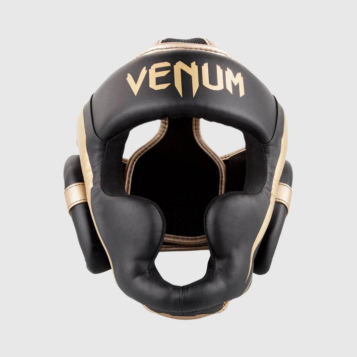 Front-facing image of the Venum Elite headgear in black with gold detailing, showcasing full face coverage including cheek and jaw protection.
