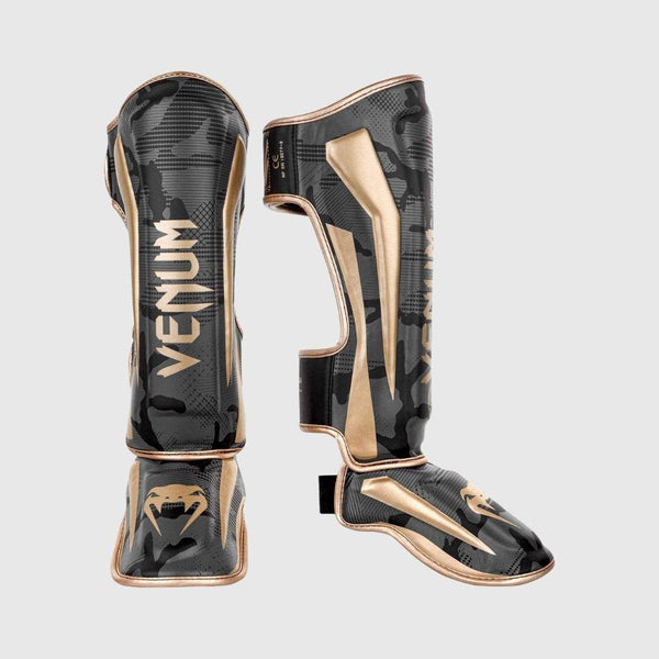 Front and side view of Venum Elite Standup Shin Guards in black camo with gold accents, showing full leg and foot protection with VENUM branding.