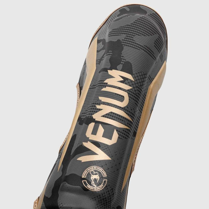 Close-up of the shin area, displaying the bold gold "VENUM" logo on a textured black camouflage surface.