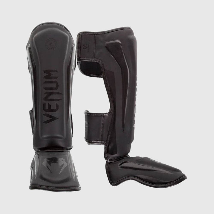 Side-by-side view of Venum Elite blackout shin guards in all black, with matte and gloss finishes.