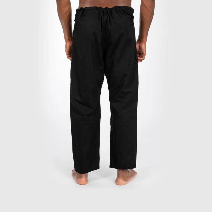 Back view of the black gi pants worn by the model, showing straight-leg fit and elastic waistband detailing.