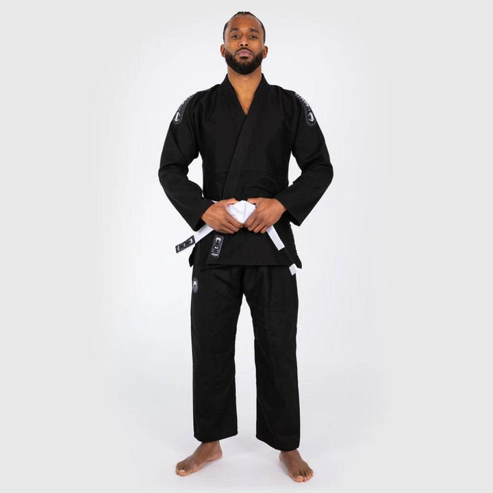 Full-body front view of the model holding his belt while wearing the complete black BJJ Gi set, giving a head-to-toe look at the outfit.