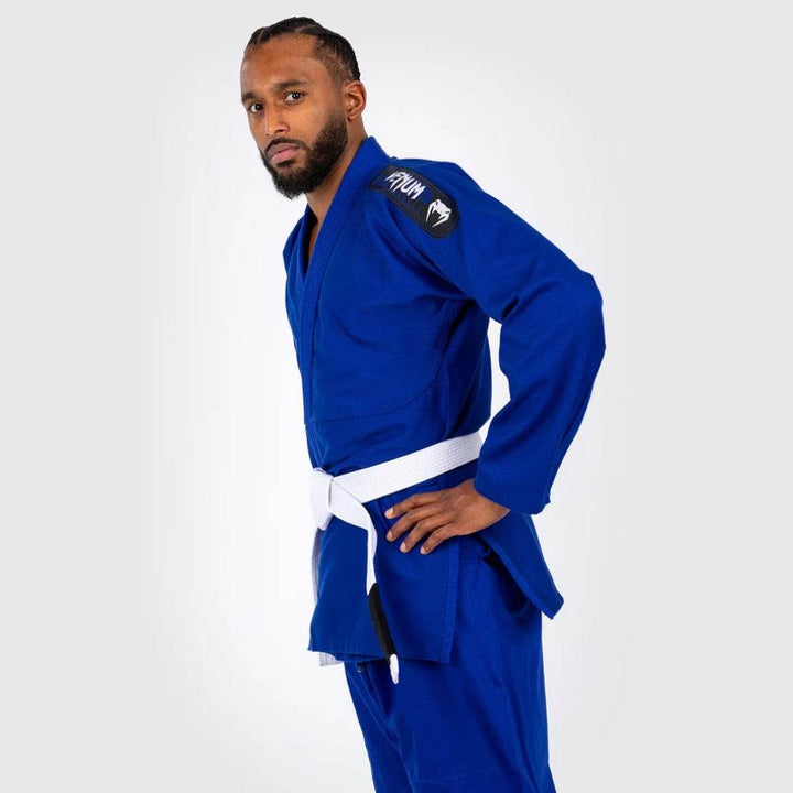 Opposite side profile of model in blue Gi with white belt, hands resting on hips, displaying patch and sleeve details.