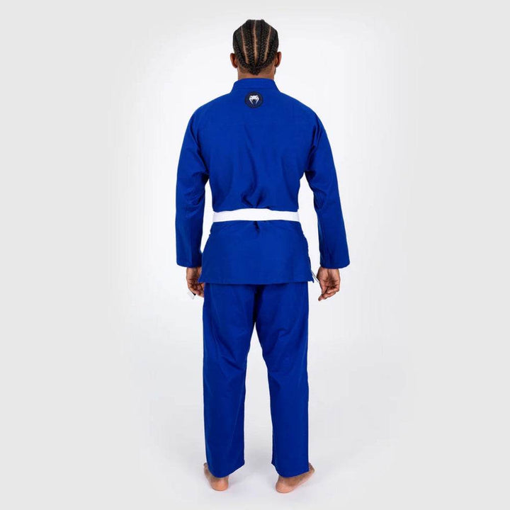 Rear view of male model standing straight in blue BJJ Gi, showing full back design and Venum logo at collar.