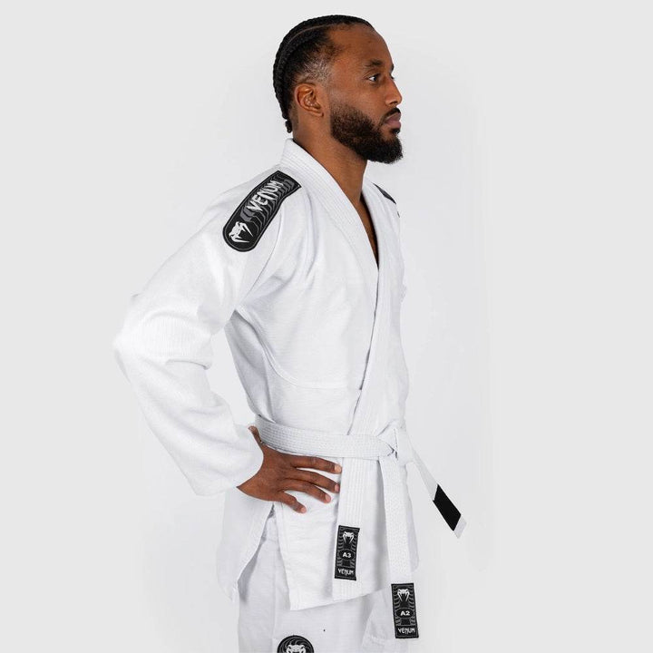 A side profile of the athlete in the white Venum BJJ gi, with hands on hips and the black shoulder Venum logo clearly visible.