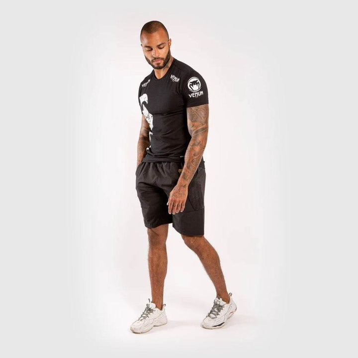 Model in black Venum t-shirt and black shorts standing in a relaxed pose.