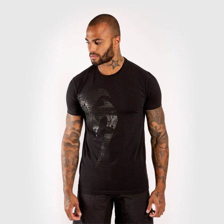 Man in black t-shirt featuring a subtle glossy Venum snake logo print on the front, standing facing forward with arms relaxed.