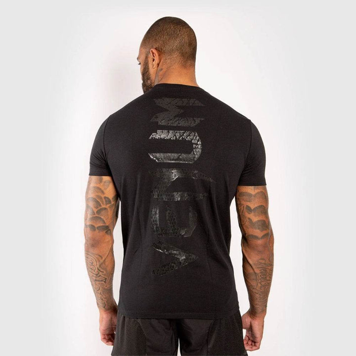 Back view of t-shirt showing large glossy black “VENUM” print running vertically down the spine.