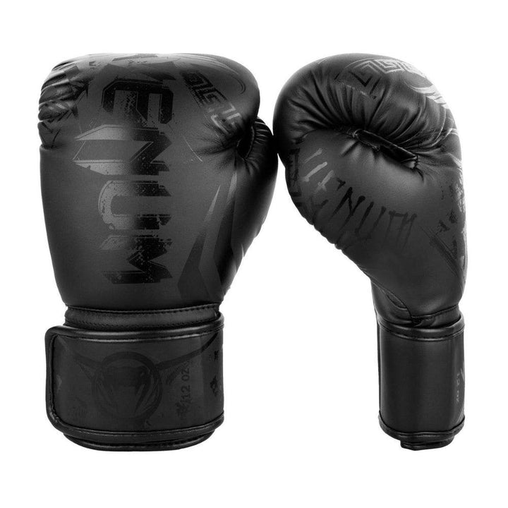 Front-and-side view of all-black Venum Gladiator 3.0 boxing gloves, upright, showing tonal Spartan-helmet graphic across knuckles.