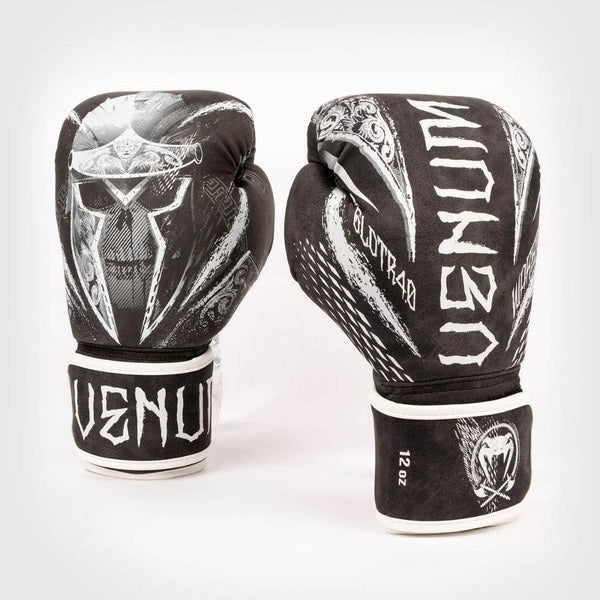 Front display of Venum Gladiator 4.0 boxing gloves, matte black with bold white Spartan-skull graphic and rough-edge “VENUM” wrist logo.