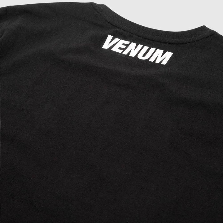 Zoomed-in image of the upper back of a black Venum t-shirt highlighting the white “VENUM” logo placed just below the collar.