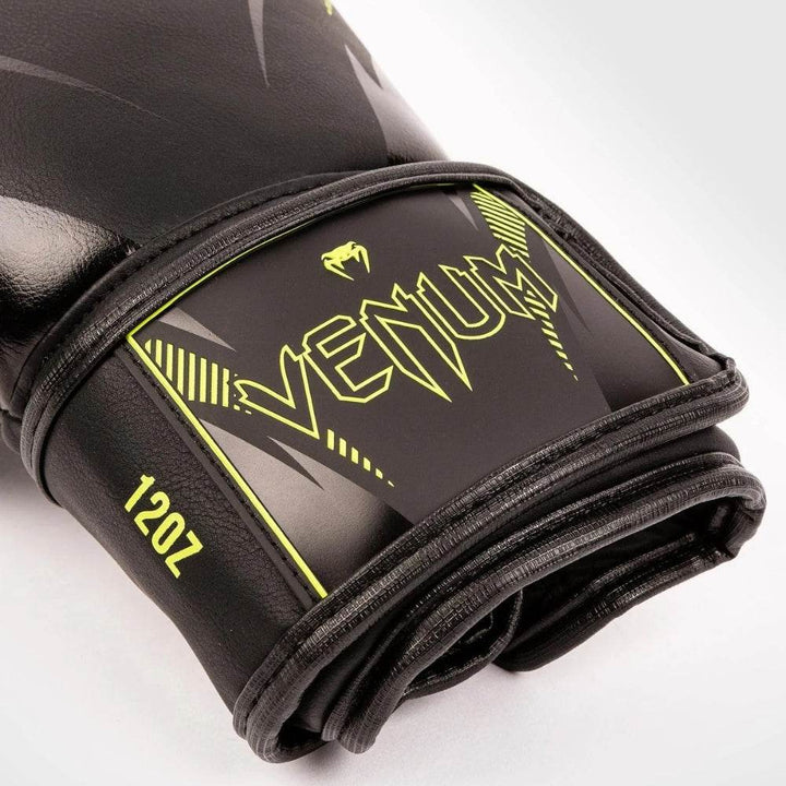 Detailed shot of the wrist area showing the "Venum" logo, 12oz weight marking, and neon yellow graphic design on the glove’s velcro strap.