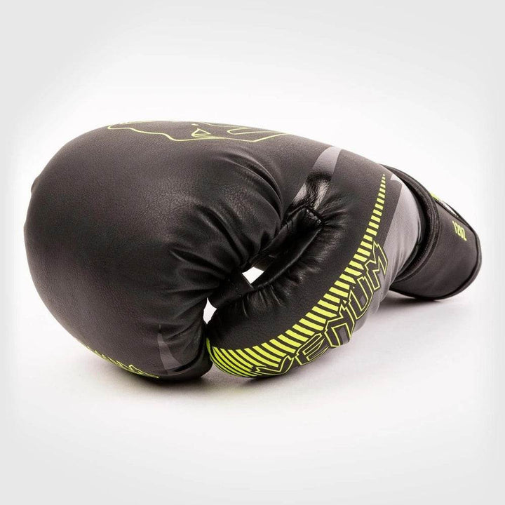 Side view of a single curled Venum Impact glove lying on its side, emphasizing the contour and stitching detail with yellow branding.