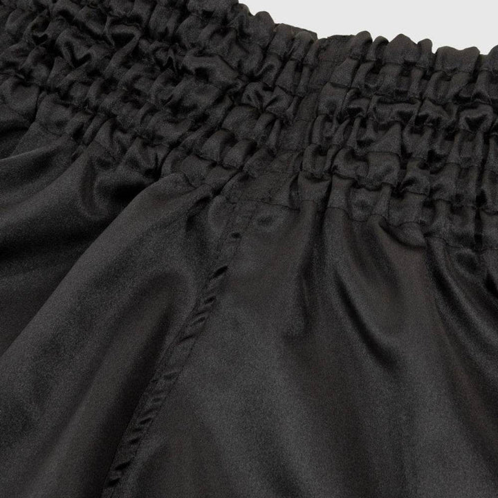 Smooth black satin fabric texture of the shorts’ waistband and body.